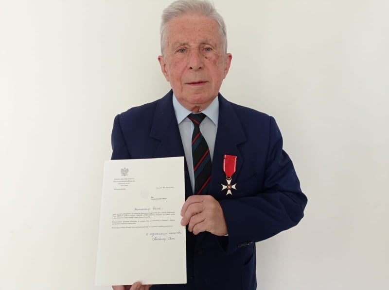 Siwy starszy Pan w garniturze trzymający list gratulacyjny